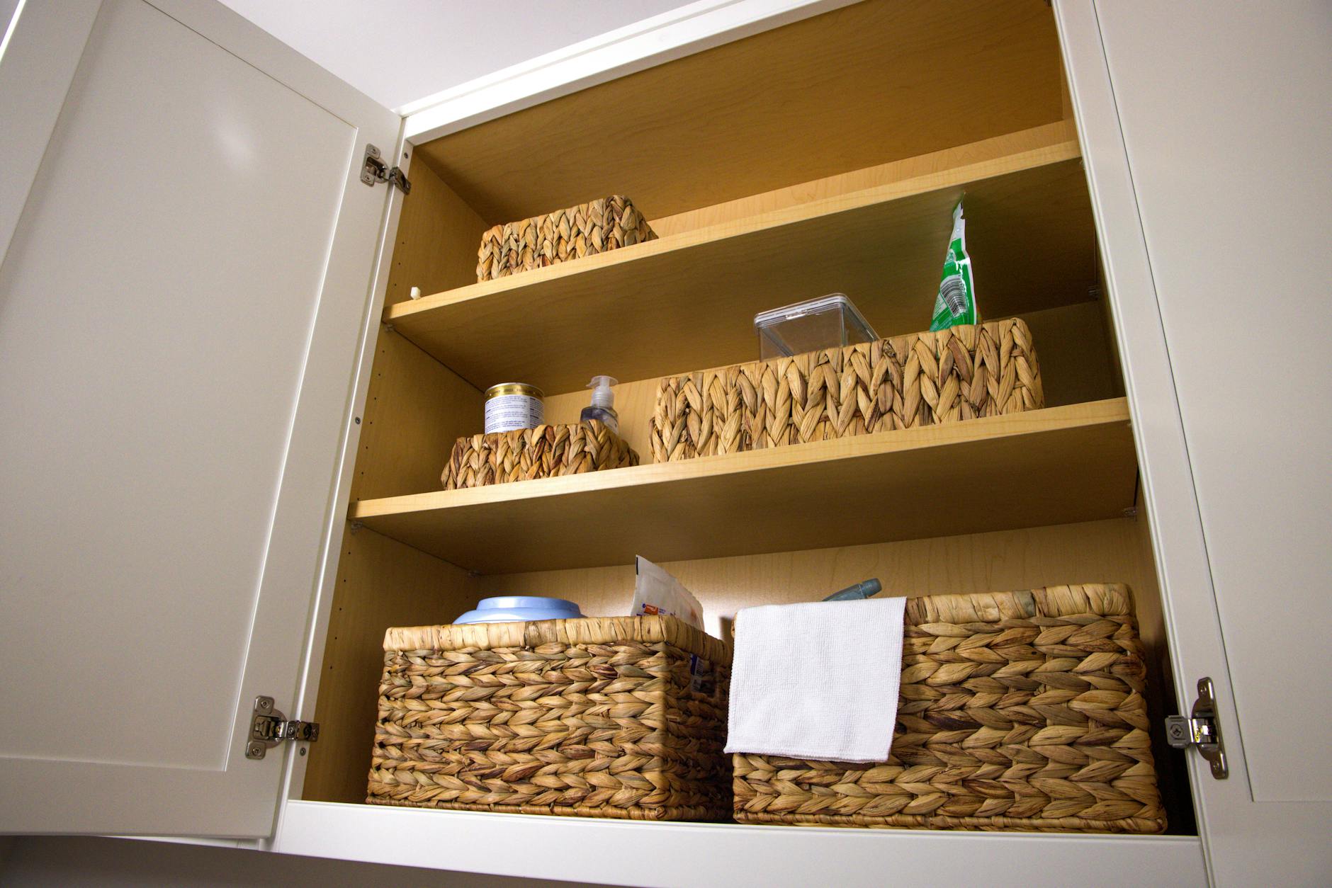 Open cabinet with three shelves holding woven baskets and small household items