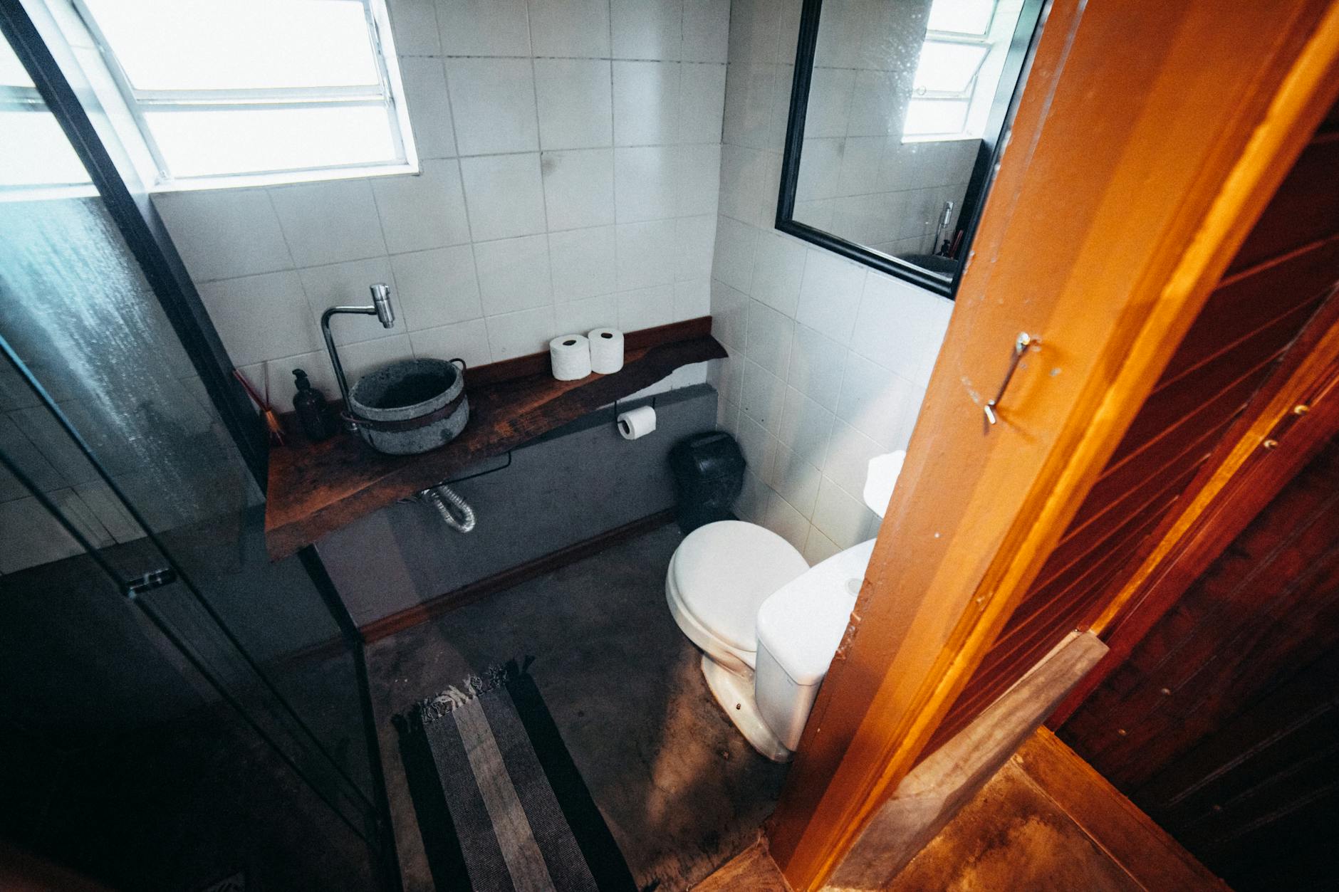Small bathroom seen from the doorway with a toilet, a stone basin on a wooden shelf, a mirror and a glass shower