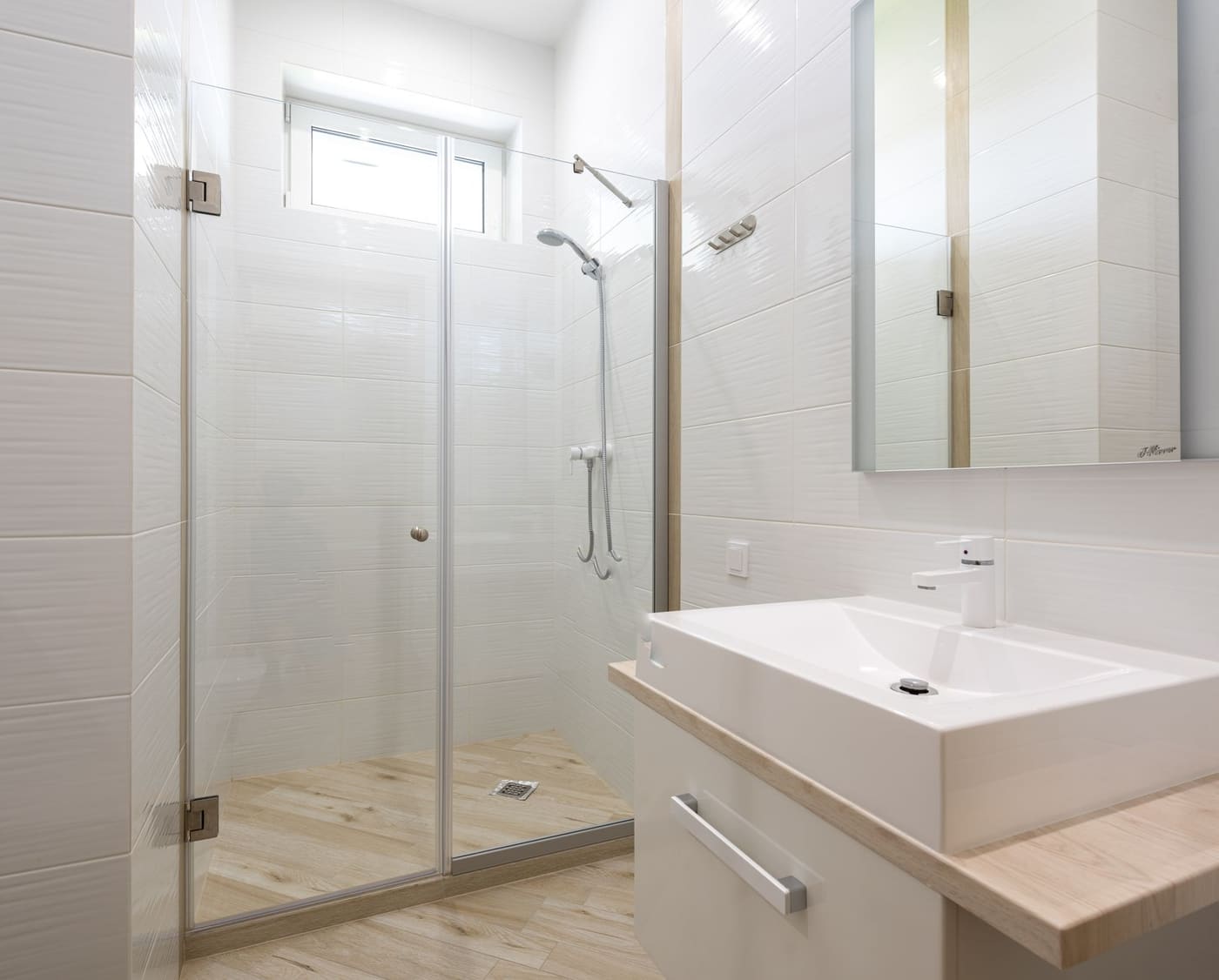 White sink and cabinet on the wall beside a shower enclosed by a transparent glass panel