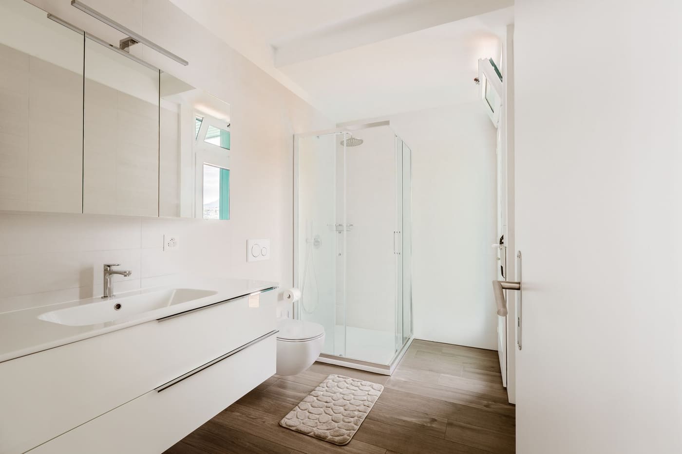 Bright bathroom with a floating white vanity, a mirror cabinet and a corner glass shower