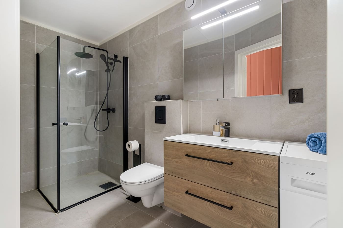 Compact bathroom with a glass-enclosed shower, a wall-hung toilet and a wood-fronted vanity under a mirror