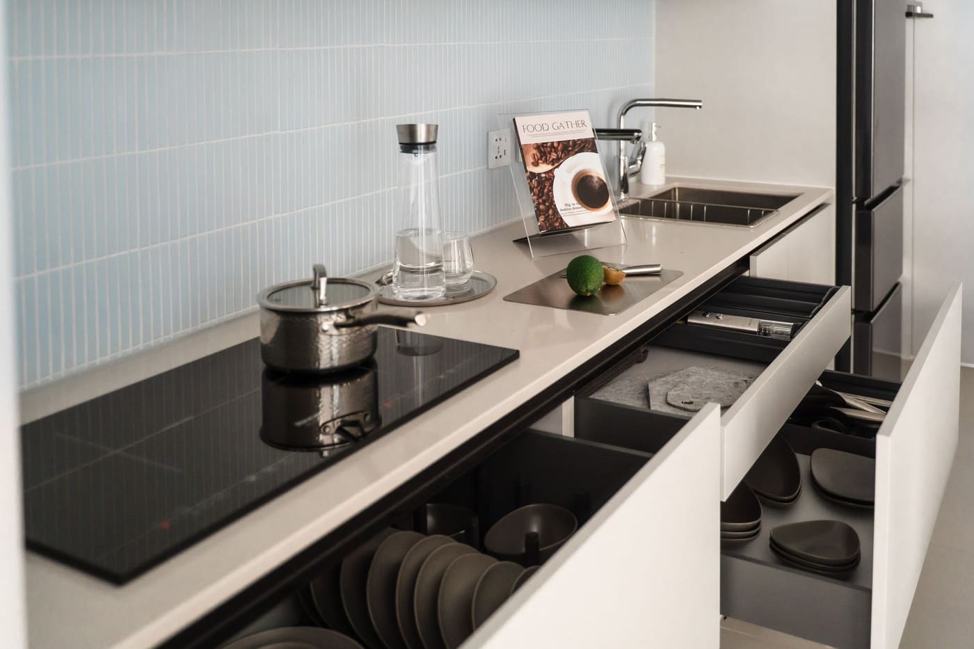 Compact kitchen counter with a black induction hob and open deep drawers holding plates and pans