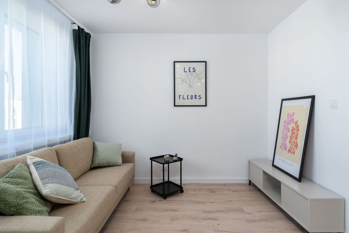 Small light room with a beige sofa, a narrow black side table and a low cabinet along the wall
