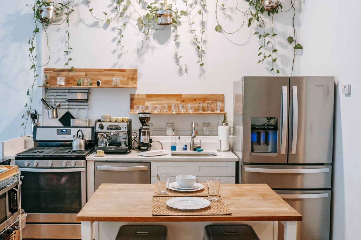 Open kitchen with a stainless refrigerator and range, open wooden shelves with plants and a small wooden table with two place settings
