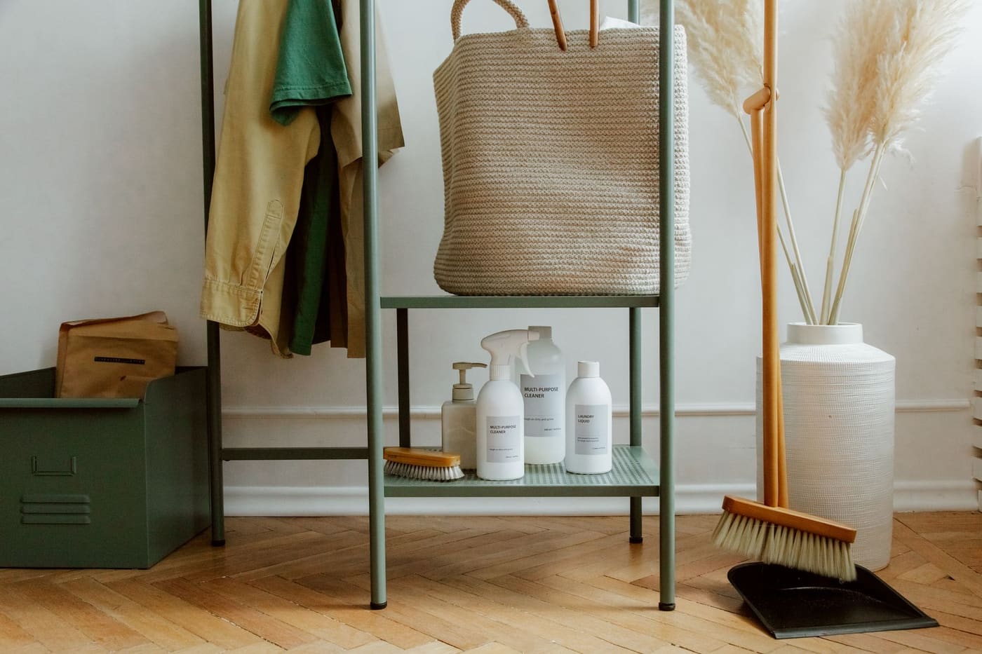 Open metal rack with a hanging bag, coats, a lidded basket and labeled bottles on the lower shelf