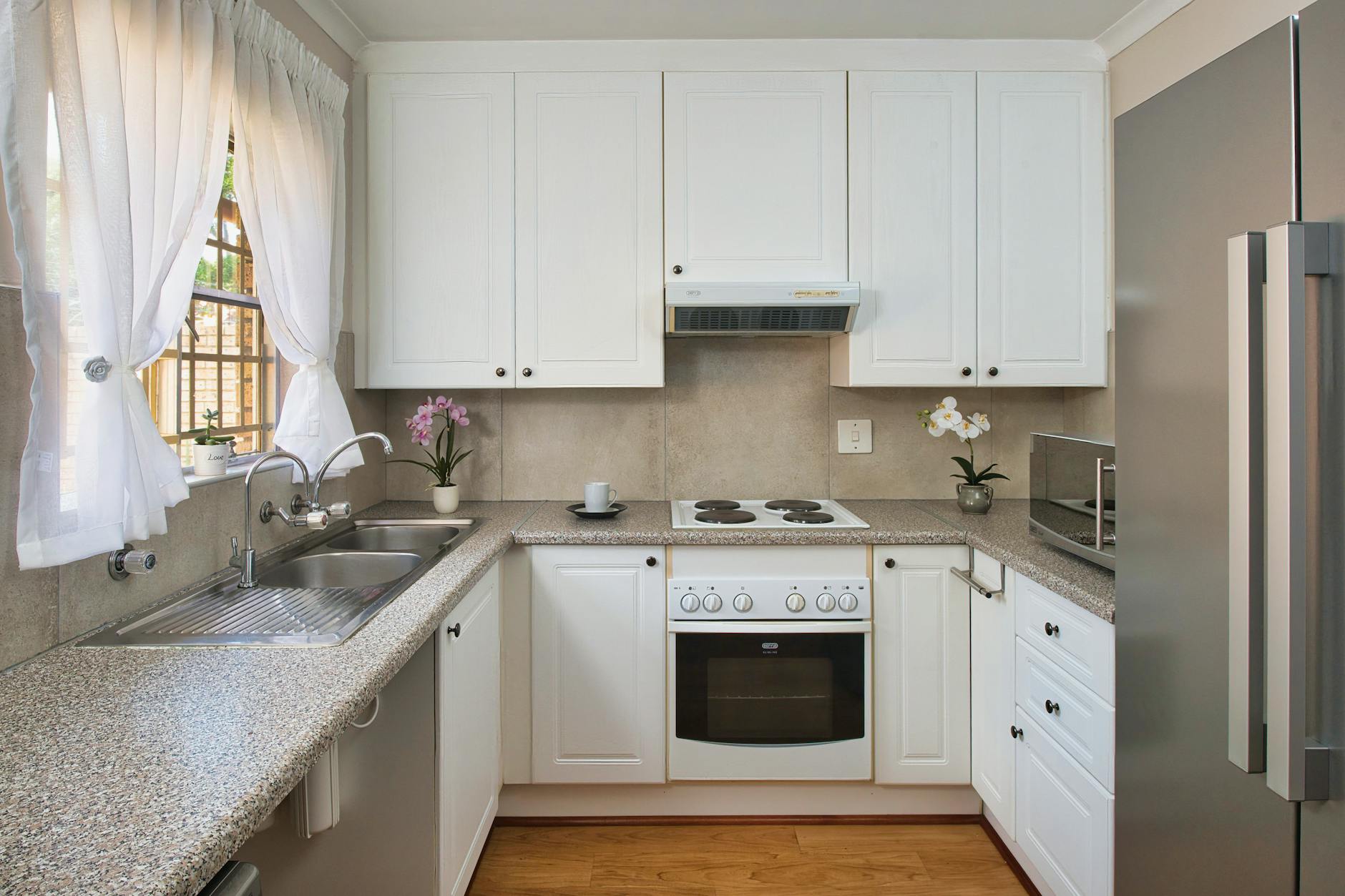 Small white U-shaped kitchen with a sink under a window, an electric hob, an oven and a tall refrigerator
